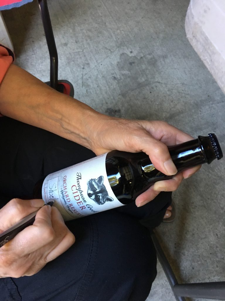 A woman writing on a bottle of beer.